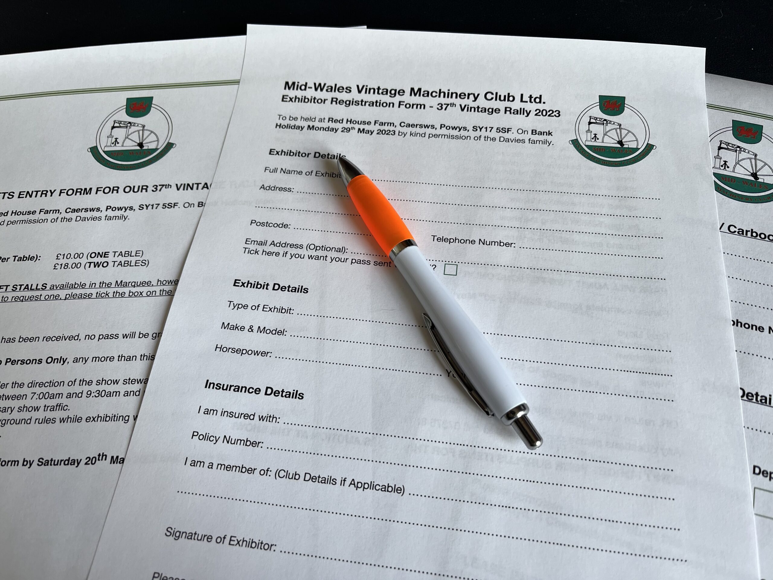 Registration forms for the Caersws Vintage Rally layed out on a table with a orange pen resting on the top of them.